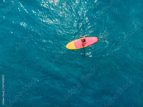 Attractive woman in swimwear floating on stand up paddle board on a quiet blue ocean. Sup surfing in tropical sea