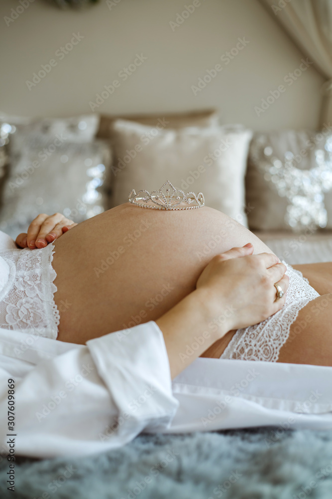 Pregnant woman in a bedroom, dressed in white lingerie.