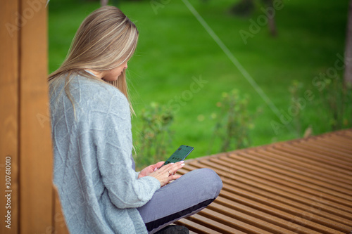 Blonde girl sits with legs on a bench and looks into a smartphone
