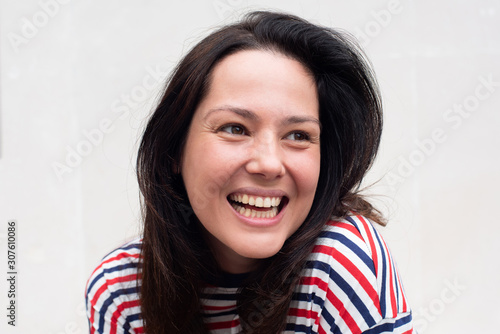 Close up happy young woman laughing by white background and looking away