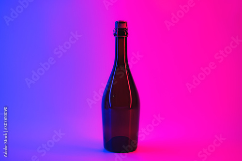 Uncorcked bottle of sparkling wine in neon background. Alcoholic beverage in vibrant lights, the concept of partying, holidays and drinking