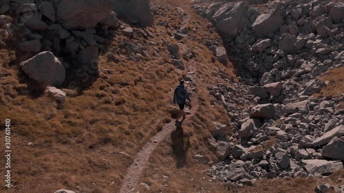 Aerial view following hiking man on arduous path in rocky mountain