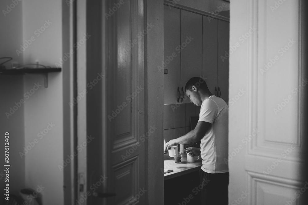 Loving husband is preparing a coffee in kitchen for his wife, side view through door. The Valentine's Day Concept. Celebrating holiday. Lifestyle. Black and white photo. Women's Day, eighth of March. Loving husband is preparing a coffee in kitchen for his wife, side view through door. The Valentine's Day Concept. Celebrating holiday. Lifestyle. Black and white photo. Women's Day, eighth of March.