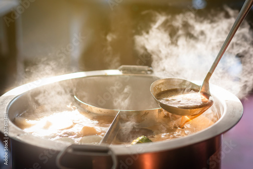 Cooking person in the restaurant is cooking while using the dipper in a large soup pot. And the water is boiling, there is smoke and hot spit.