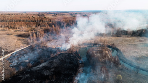 Flying over a fire in the forest. Black burned field, there is a strong thick smoke. A small river blocks the path of fire.