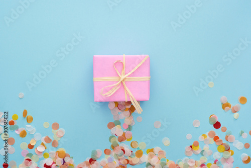 top view of pink present with bow near colorful confetti on blue