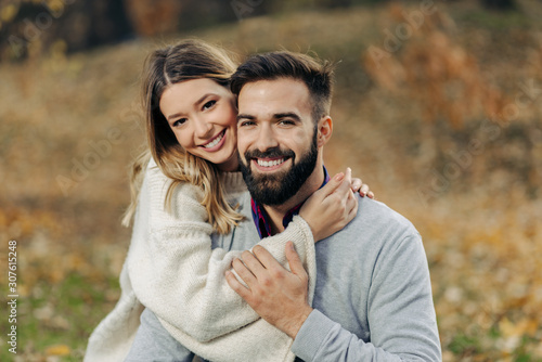 Young loving couple enjoying embraced in autumn day and looking at camera