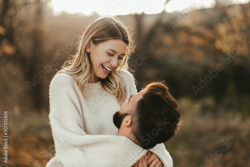Young cheerful couple having fun in nature during autumn. Woman being carried by her boyfriend