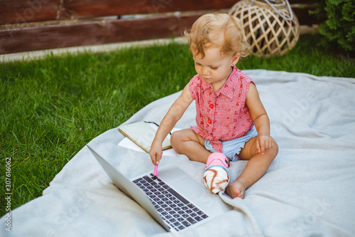 little girl types on the laptop on the green grass. © CRISTINA