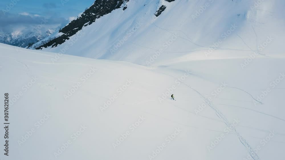Aerial shot side view professional male snowboarder ride on empty track at ski resort. Extreme long shot male enjoying winter activities surrounded by high mountain and snow Aerial shot side view professional male snowboarder ride on empty track at ski resort. Extreme long shot male enjoying winter activities surrounded by high mountain and snow