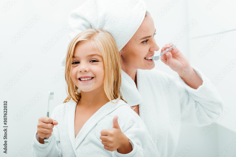cute child holding toothbrush and showing thumb up near mother cute child holding toothbrush and showing thumb up near mother