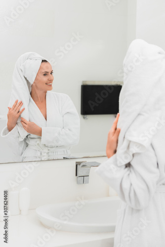 attractive woman in bathrobe looking at mirror in bathroom