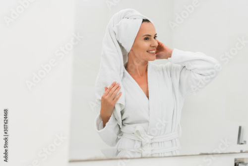 cheerful woman in bathrobe and towel looking at mirror
