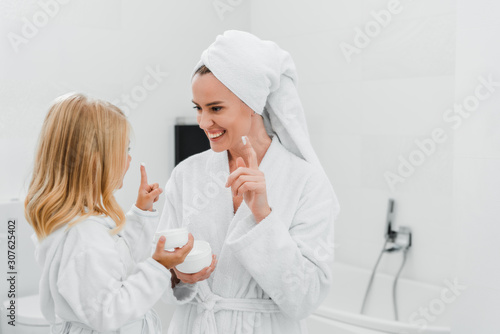 cheerful mother and daughter with face cream on fingers
