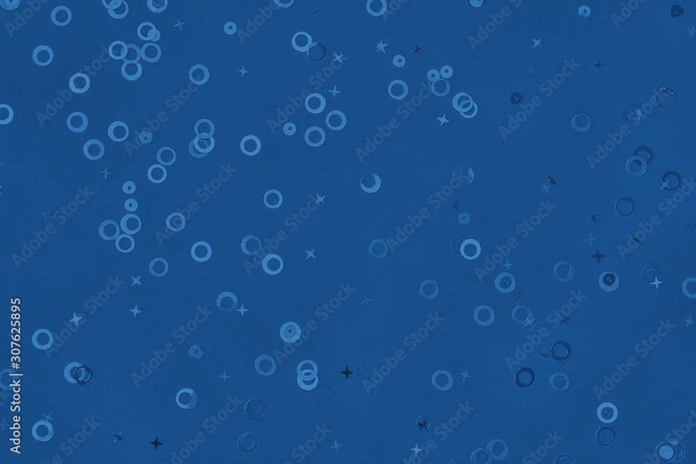 Monochrome metallic foil confetti background. Trendy classic blue colored circles and stars sparse on dark blue green colored paper. Simple holiday concept. Top view, flat lay. Color of the year 2020