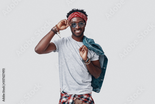 Handsome young African man adjusting his eyewear and looking at camera while standing against grey background