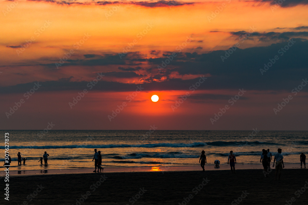 Sunset on the island of Bali, Indonesia. People walk on the beach.