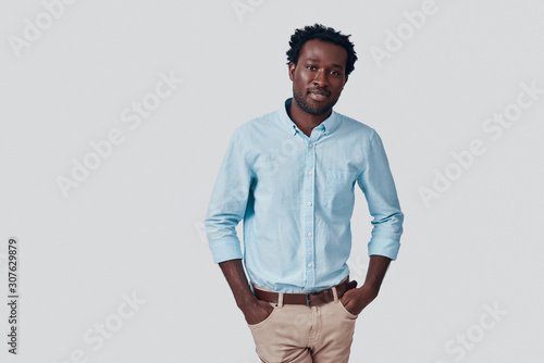 Handsome young African man looking at camera and smiling while standing against grey background