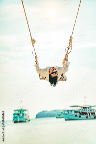 Gorgeous young woman is swinging on a swing which hangs on a tree and enjoying the beautiful summer weather on the Phu Quoc island, Vietnam.