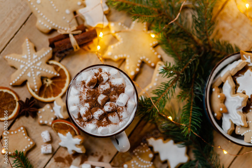 Winter hot drink: white mug with hot chocolate with marshmallow and cinnamon. Cozy home atmosphere, festive holiday mood. Rustic style, wooden background. Homemade gingerbread cookies. Flat lay