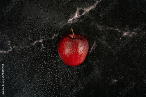 fresh red apple with drops of water lies on a black marble background full of water spray droplets. Top view flat lay composition.
