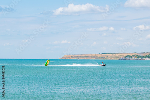Speed tubing with a jet ski. Donut turn up and fly over the sea. Nice seascape on the background. Light blue sky and azure, baby blue water. Copy space. 