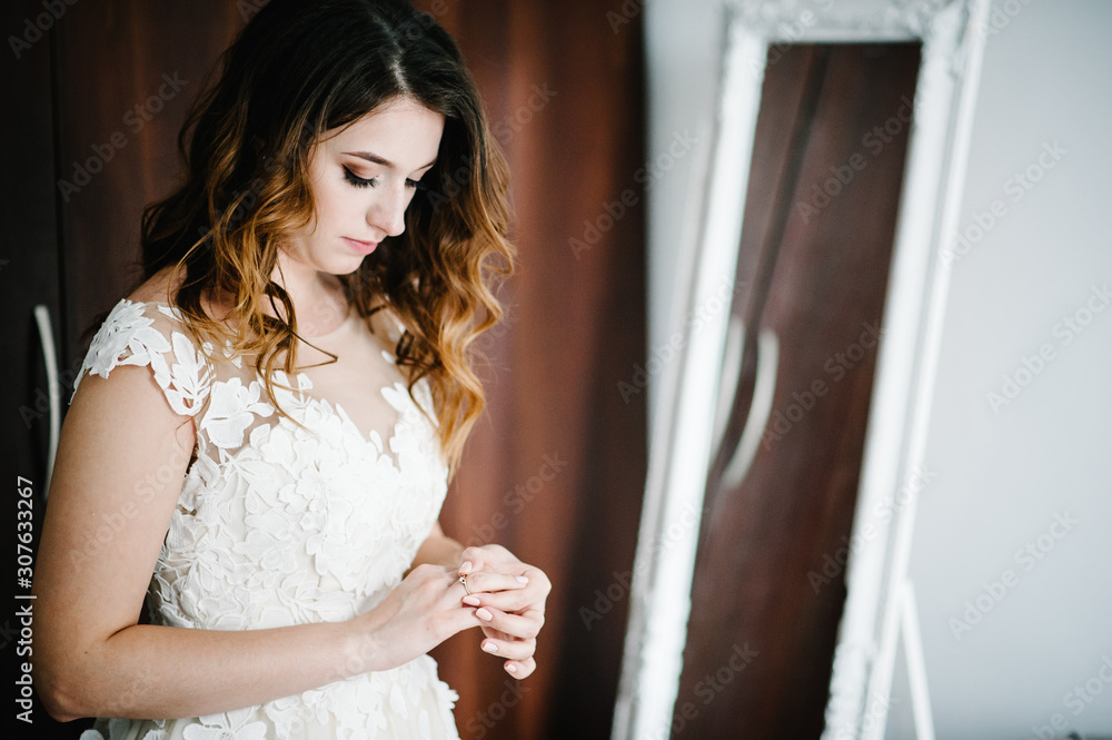 An attractive bride in a wedding dress wearing and corrects a gold wedding engagement ring. Bride's Preparations. Wedding Morning.