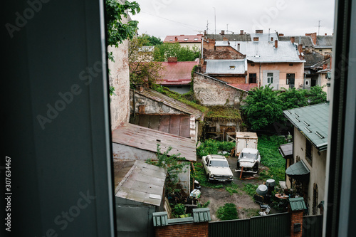 Artwork, noise, grain. View through the window to the old city, retro cars, abandoned houses and overgrown greens.
