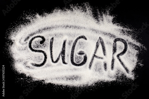 Word sugar  hand lettering on black background. The text on powdered white granulated sugar. Sugar eating harm concept