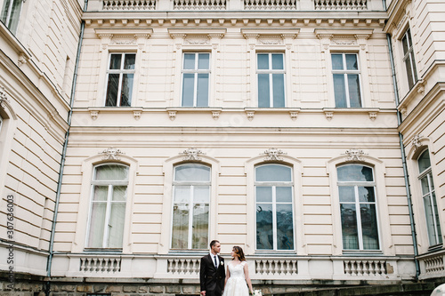 Portrait the groom and bride stand near ancient restored architecture, old building, old house outside, vintage palace outdoor. Romantic love in vintage atmosphere street. photo