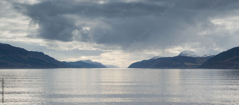 A view across Loch Ness looking down the length of the lake with rocks inn the foreground and dark clouds above, in Scotland, UK