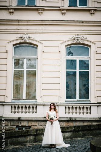 Portrait bride in wedding dress with a bouquet of flowers standing in old city near the palace. © Serhii