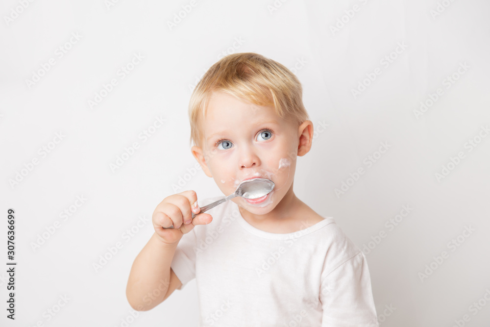 portrait of a blond blue-eyed little caucasian cute boy eating a yogurt with a spoon on a white background portrait of a blond blue-eyed little caucasian cute boy eating a yogurt with a spoon on a white background