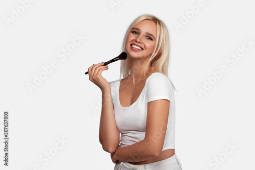 Beautiful blonde girl applies skin tone with Brush. Sexy woman portrait isolated on white background. Perfect Makeup. Skincare Foundation. Pretty girl with perfect skin smiling. Brushes Makeup Artist.