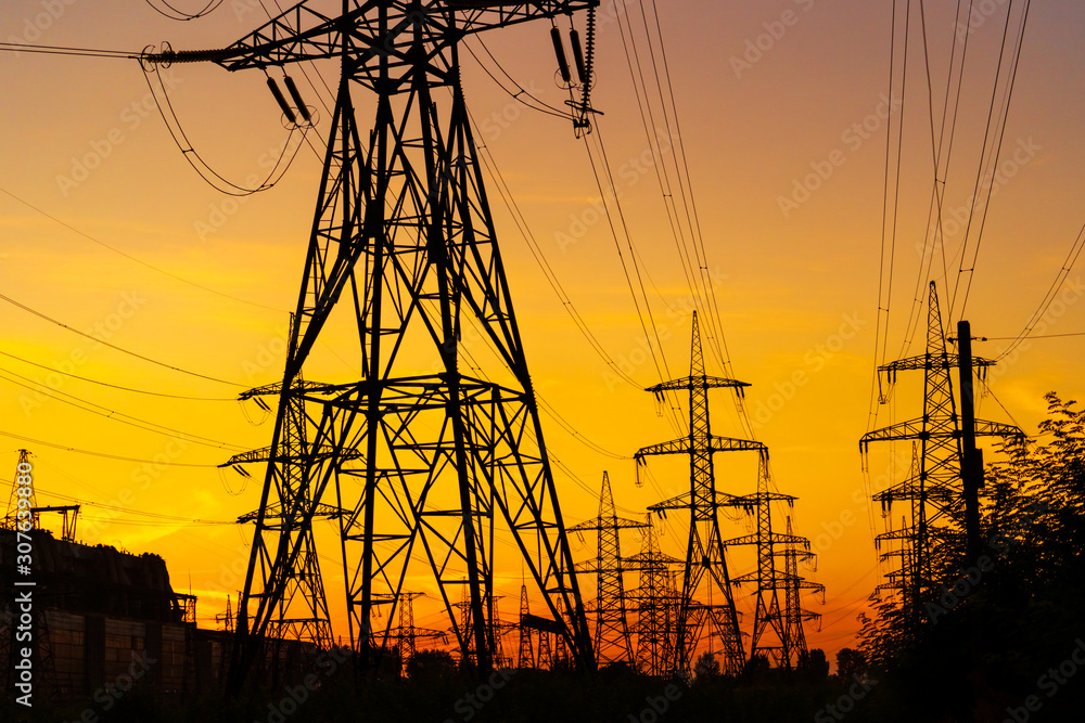 Electricity pylons bearing the power supply across a rural landscape during sunset. Selective focus.