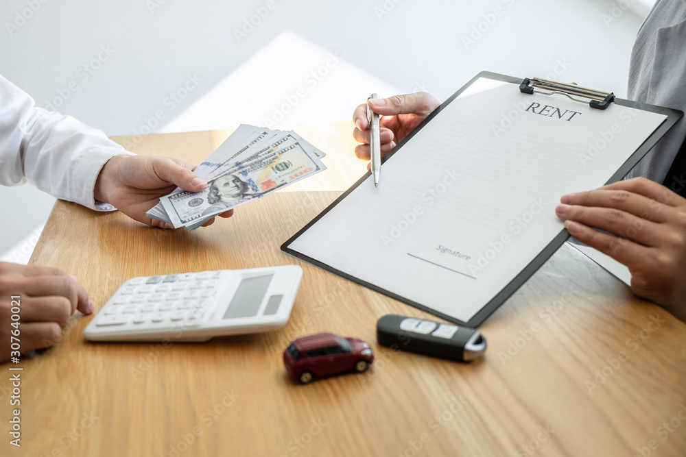 Car rental and Insurance concept, Young salesman receiving money and giving car's key to customer after sign agreement contract with approved good deal for rent or purchase Car rental and Insurance concept, Young salesman receiving money and giving car's key to customer after sign agreement contract with approved good deal for rent or purchase