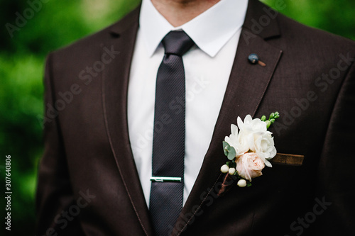 The groom wiht boutonniere or buttonhole on the jacket, is stands on the background greenery in the garden.