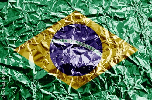 Brazil flag depicted in paint colors on shiny crumpled aluminium foil closeup. Textured banner on rough background