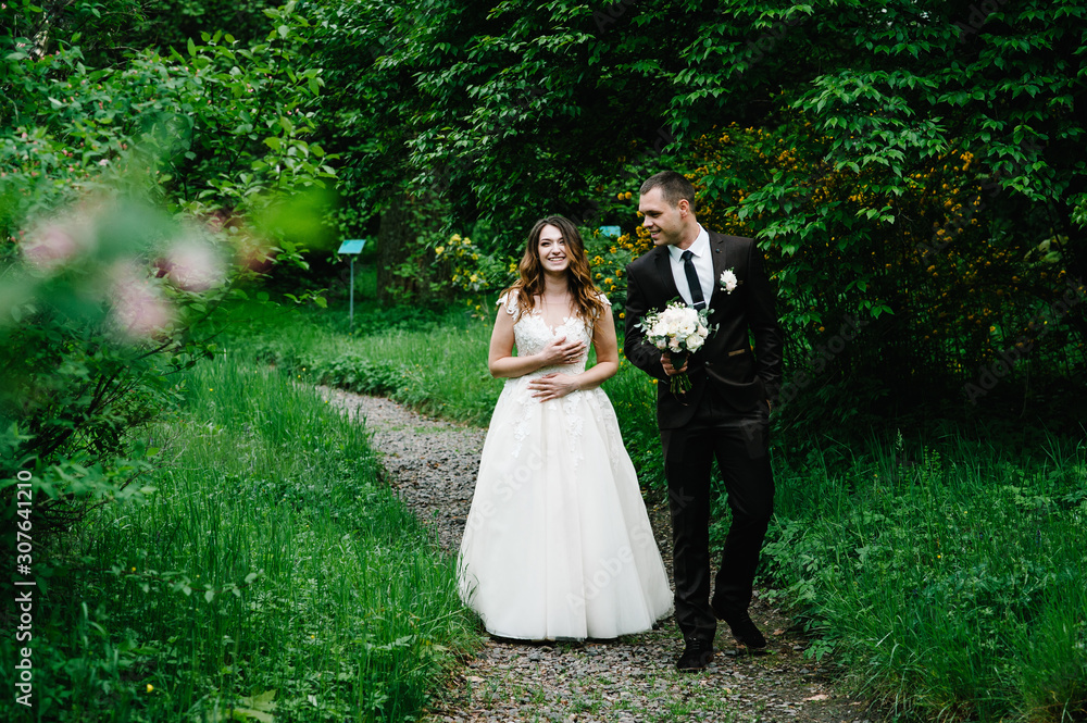 Attractive couple newlyweds is walking on a trail in an green forest. Happy and joyful moment.