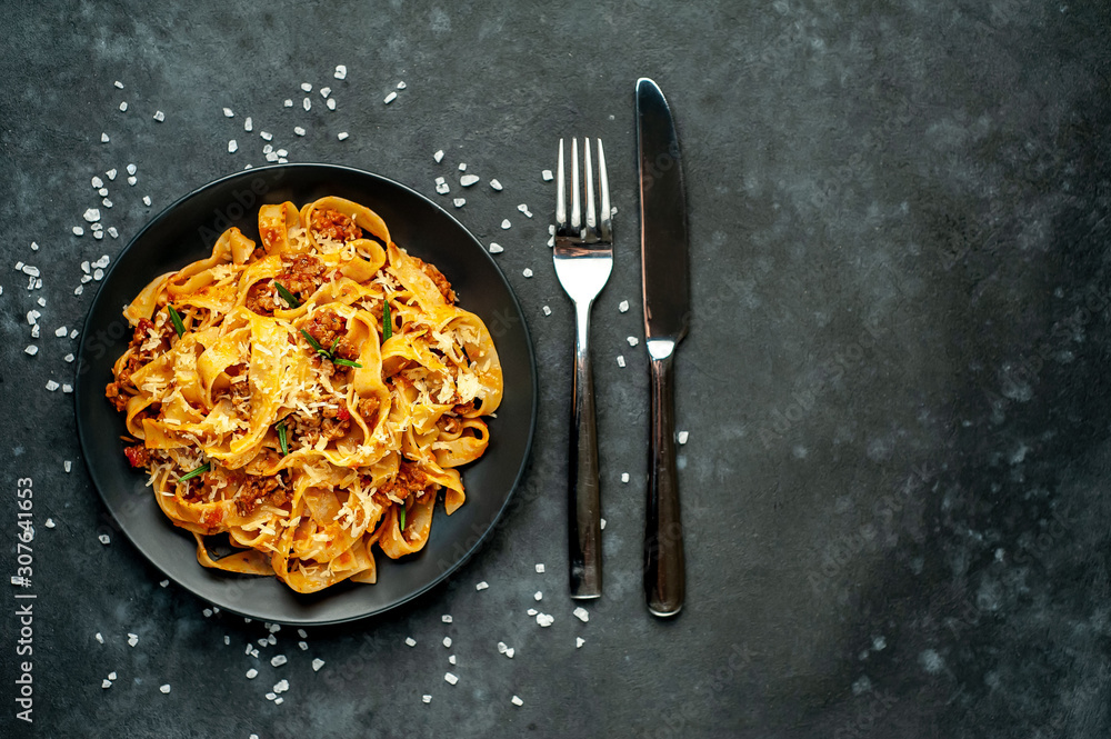 Pasta Bolognese with spices, Italian pasta dish with minced meat and tomatoes in a dark plate on a stone background with copy space for your text - obrazy, fototapety, plakaty 