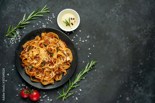 Pasta Bolognese with spices, Italian pasta dish with minced meat and tomatoes in a dark plate on a stone background with copy space for your text