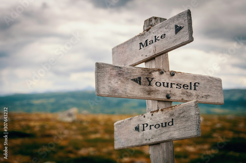 фотографія Make yourself proud text quote on wooden rustic signpost outdoors in nature/mountain scenery