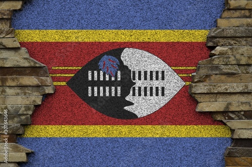 Swaziland flag depicted in paint colors on old stone wall closeup. Textured banner on rock wall background photo