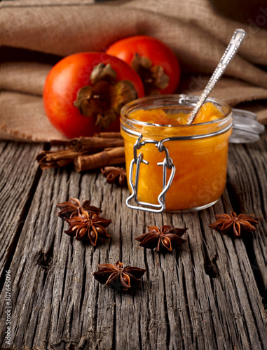 Fresh Persimmon and Persimmon jam or marmalade in glass jar on wooden background. Close up photography.