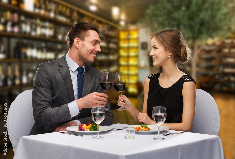 leisure and luxury concept - smiling couple with food clinking glasses of red wine over restaurant background
