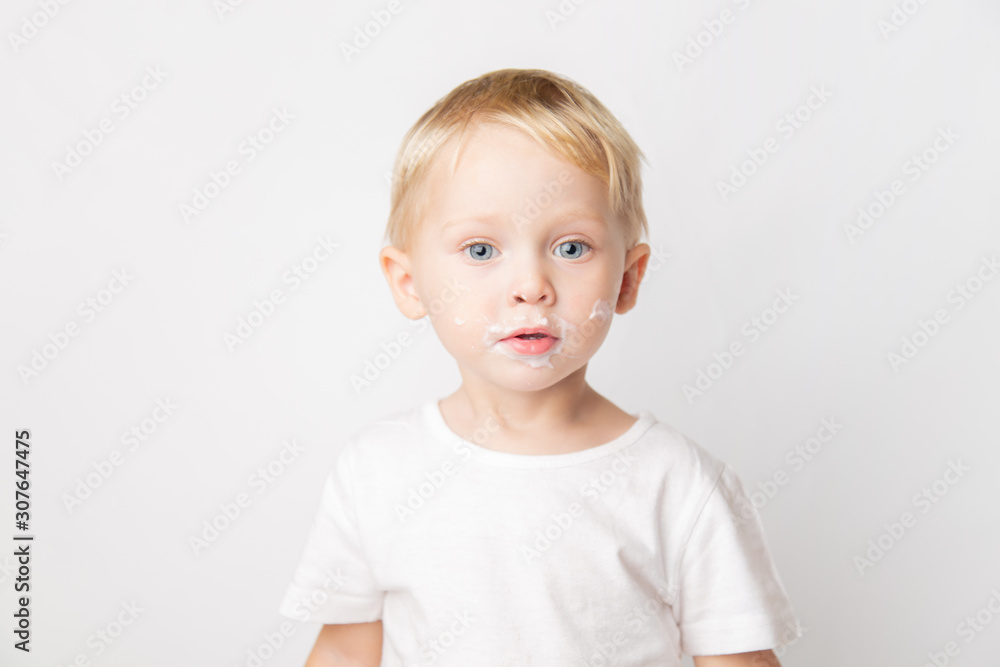 portrait of a cute caucasian blue-eyed boy with yogurt on his face on a white background. portrait of a cute caucasian blue-eyed boy with yogurt on his face on a white background.