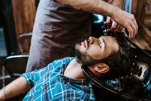 tattooed barber washing hair of bearded man with closed eyes