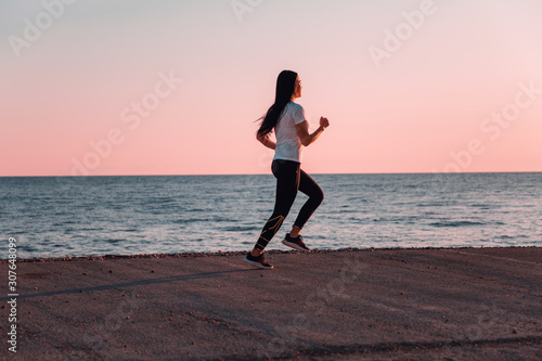 The concept of sport and running. Woman in sportswear running on the track. In the background, the sea and the horizon line. Copy space. Pink sunset