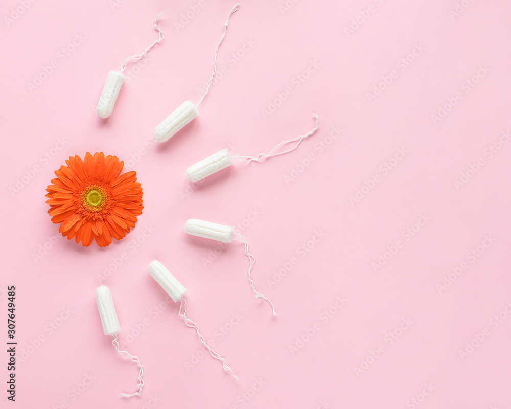 Feminine intimate hygiene set over pink background with orange flower. Menstruation sanitary soft cotton tampons. Woman hygiene protection. Flat lay, top view. Menstrual period concept. Feminine intimate hygiene set over pink background with orange flower. Menstruation sanitary soft cotton tampons. Woman hygiene protection. Flat lay, top view. Menstrual period concept.
