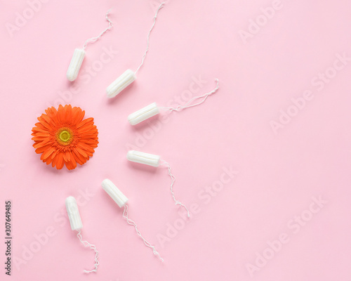 Feminine intimate hygiene set over pink background with orange flower. Menstruation sanitary soft cotton tampons. Woman hygiene protection. Flat lay, top view. Menstrual period concept.